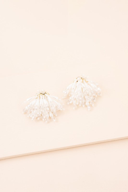 Introducing the Flare Drop Earrings—a pair of elegant white tassel earrings featuring intricate beaded details on a light background, perfect for completing a bridal ensemble. The sterling silver post adds an extra touch of sophistication.