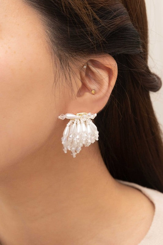 Introducing the Flare Drop Earrings—a pair of elegant white tassel earrings featuring intricate beaded details on a light background, perfect for completing a bridal ensemble. The sterling silver post adds an extra touch of sophistication.