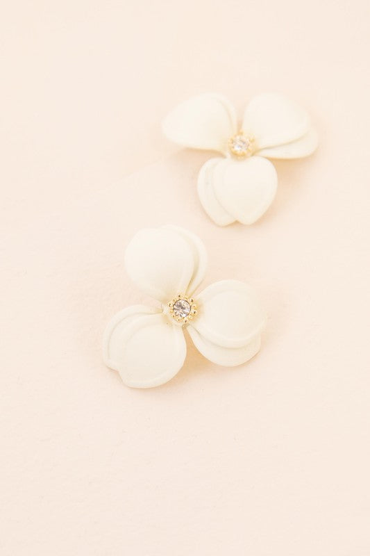 Close-up of a pair of cream-colored Gardenia Statement Earrings set against a soft beige backdrop, showcasing the intricate detail of their sterling silver craftsmanship.