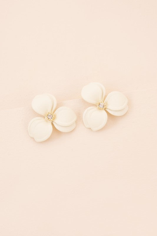 Close-up of a pair of cream-colored Gardenia Statement Earrings set against a soft beige backdrop, showcasing the intricate detail of their sterling silver craftsmanship.