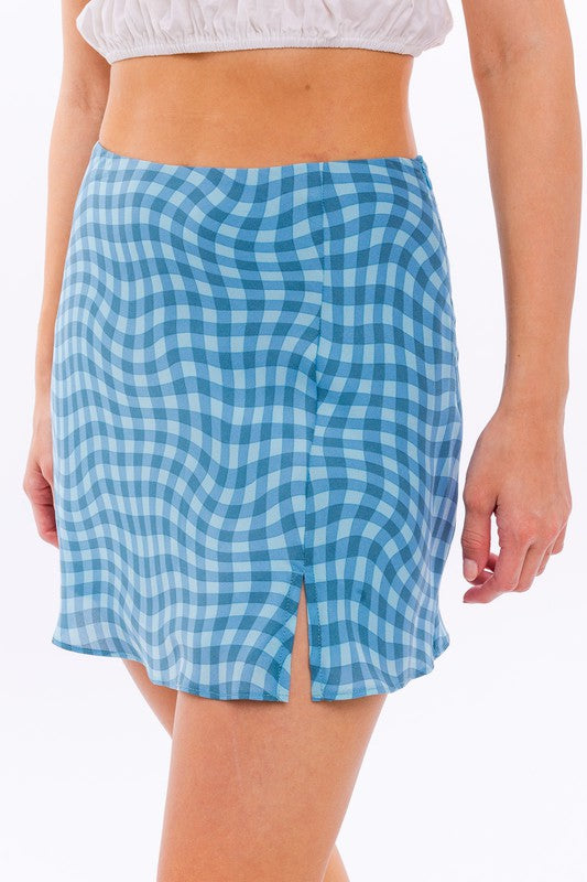 A person wears the Bias Cut Mini Skirt, featuring a trendy blue checkered print and a fashionable side slit, complemented by white cowboy boots on a pristine white background.