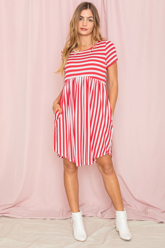 Dressed in a Plus Short Sleeve Stripe Mini Dress, a woman stands against a light pink background, gazing to the side with a slight smile.