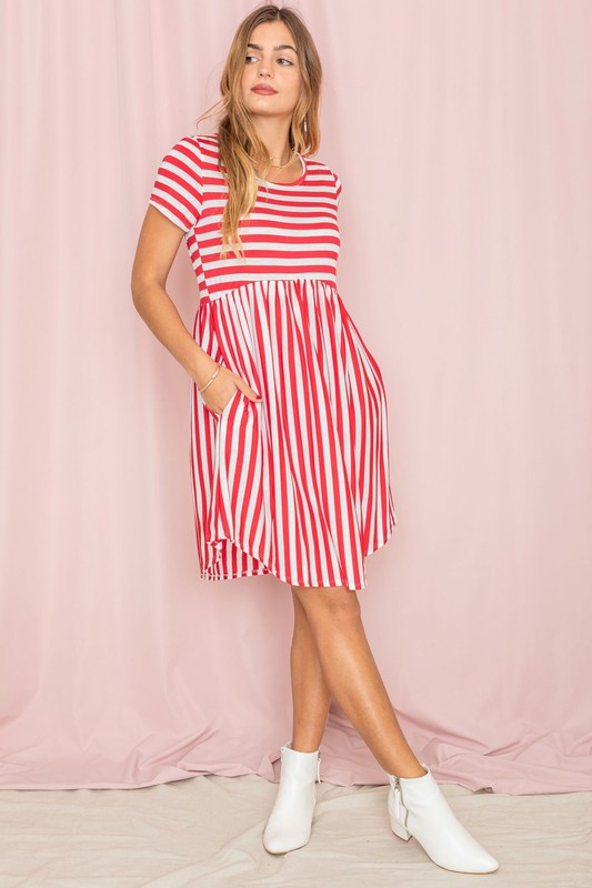 Dressed in a Plus Short Sleeve Stripe Mini Dress, a woman stands against a light pink background, gazing to the side with a slight smile.