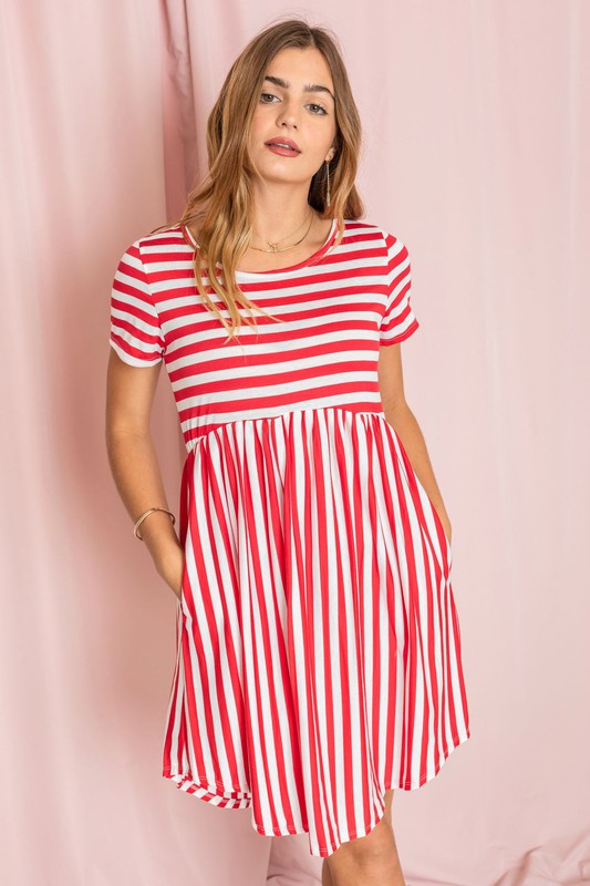 Dressed in a Plus Short Sleeve Stripe Mini Dress, a woman stands against a light pink background, gazing to the side with a slight smile.