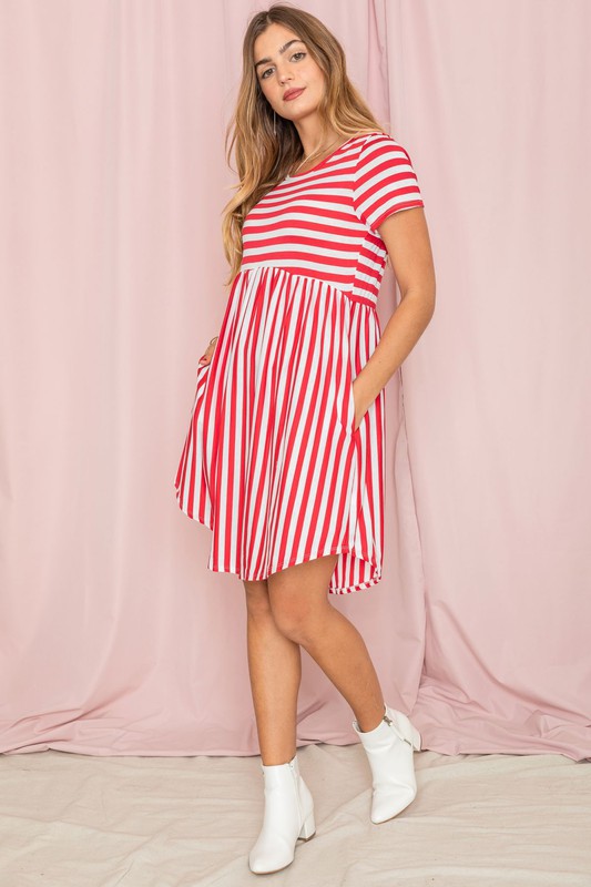 Dressed in a Plus Short Sleeve Stripe Mini Dress, a woman stands against a light pink background, gazing to the side with a slight smile.