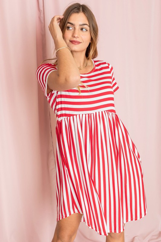 Dressed in a Plus Short Sleeve Stripe Mini Dress, a woman stands against a light pink background, gazing to the side with a slight smile.