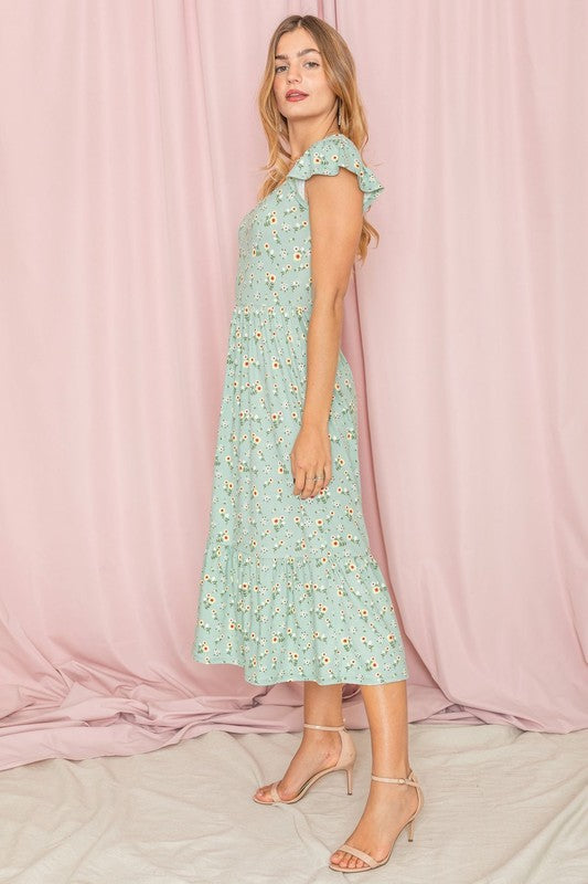 A person wearing a Flutter Sleeve Ditsy Floral Sundress stands against a pink curtain backdrop.