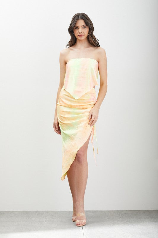 A woman stands in front of a neutral background, styled in the Strappy Back Tie Top featuring a strapless design and pastel tie-dye pattern with ruching.