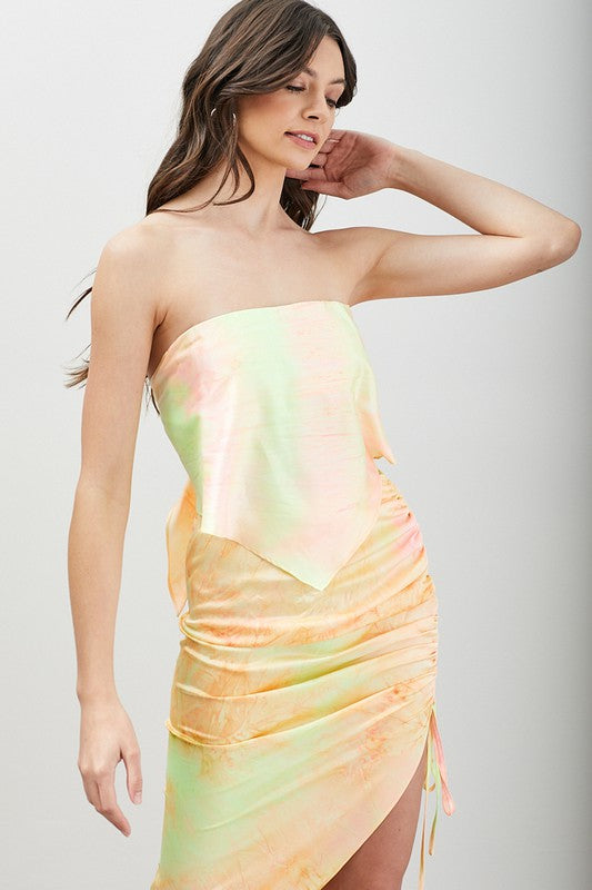 A woman stands in front of a neutral background, styled in the Strappy Back Tie Top featuring a strapless design and pastel tie-dye pattern with ruching.