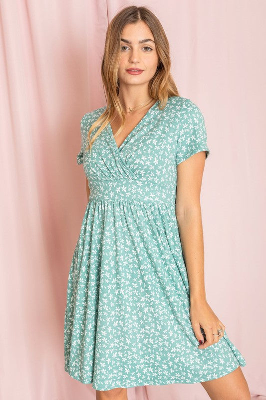 A woman elegantly models the Surplice Ditsy Floral Midi Dress, made from a comfortable polyester and spandex blend, set against a lively pink background.