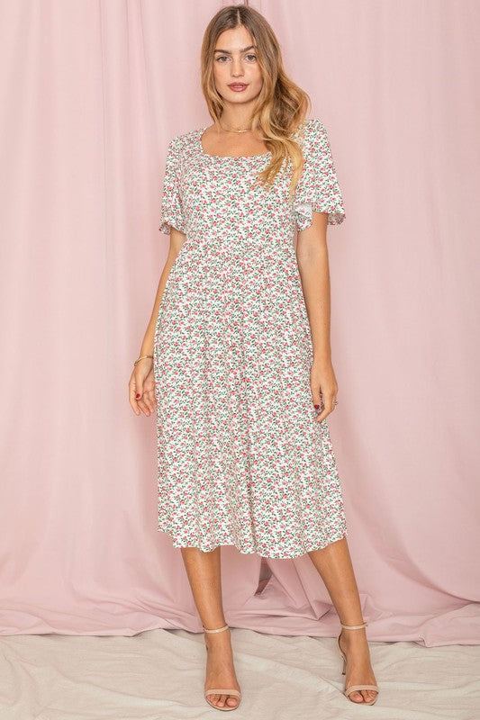 A woman stands in front of a pink backdrop, wearing the Kimono Sleeve Floral Tea Length Dress and beige heels.