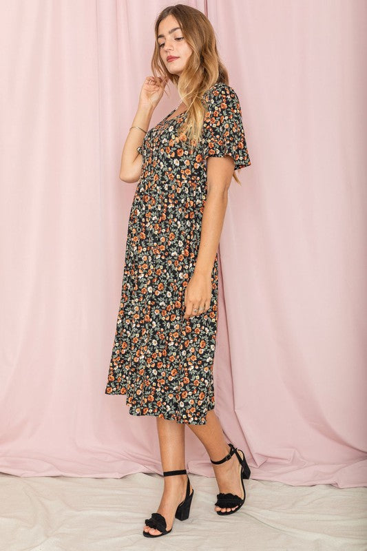 A woman stands in front of a pink backdrop, wearing the Kimono Sleeve Floral Tea Length Dress and beige heels.