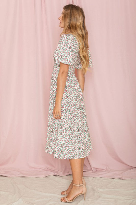 A woman stands in front of a pink backdrop, wearing the Kimono Sleeve Floral Tea Length Dress and beige heels.