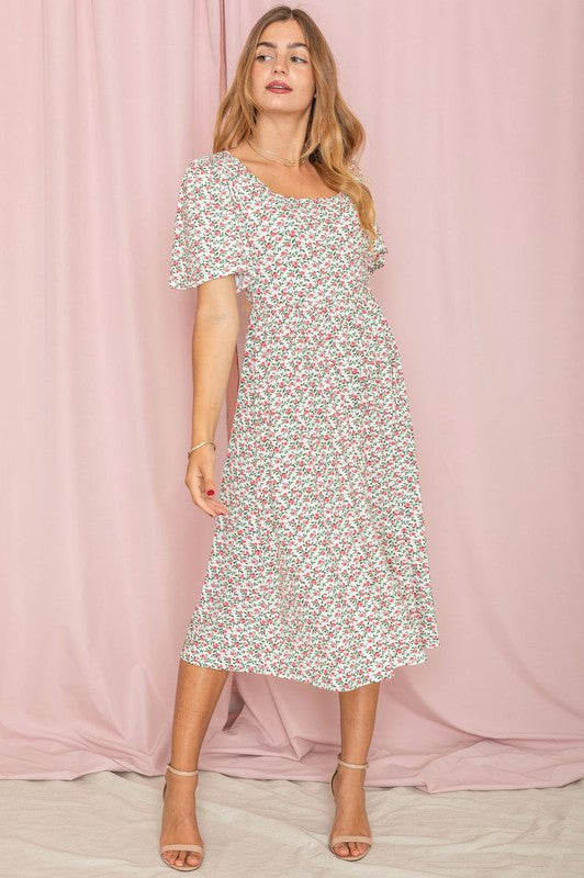 A woman stands in front of a pink backdrop, wearing the Kimono Sleeve Floral Tea Length Dress and beige heels.