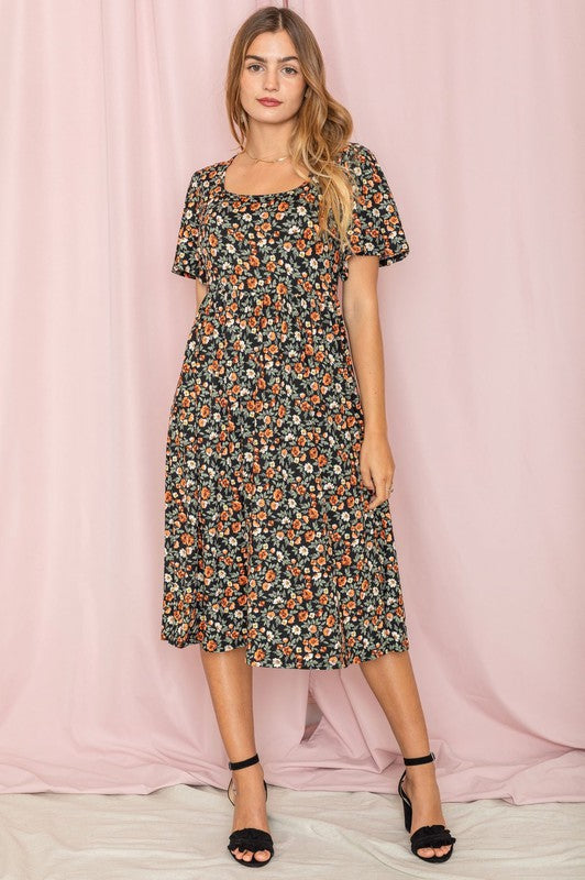 A woman stands in front of a pink backdrop, wearing the Kimono Sleeve Floral Tea Length Dress and beige heels.