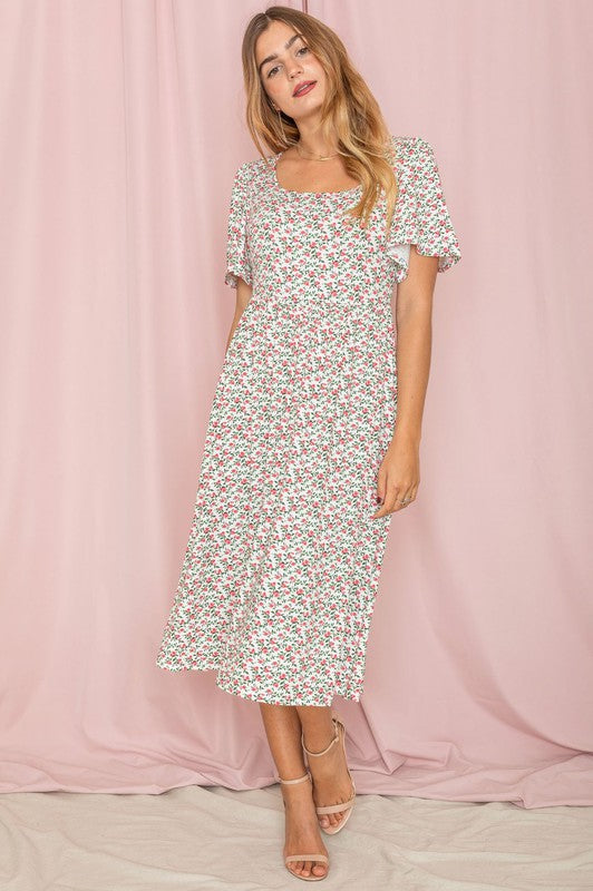 A woman stands in front of a pink backdrop, wearing the Kimono Sleeve Floral Tea Length Dress and beige heels.