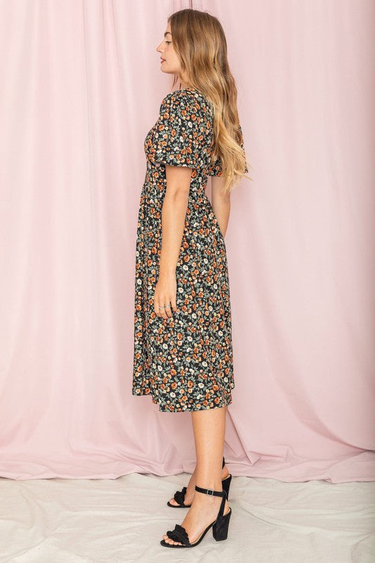 A woman stands in front of a pink backdrop, wearing the Kimono Sleeve Floral Tea Length Dress and beige heels.