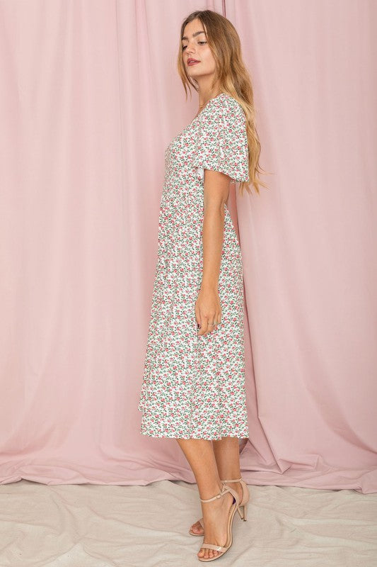 A woman elegantly wearing the Kimono Sleeve Floral Tea Length Dress and black heels stands gracefully in front of a pink curtain.