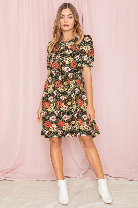 A woman in a Gathered Sleeve Daisy Floral Midi Dress stands in front of a pink curtain, delicately touching her sleeve.