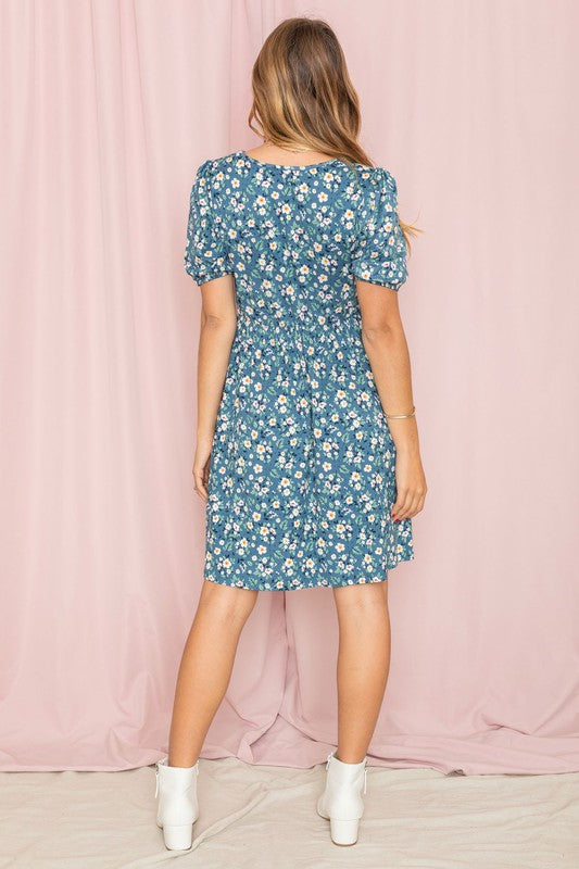 A woman in a Gathered Sleeve Daisy Floral Midi Dress stands in front of a pink curtain, delicately touching her sleeve.