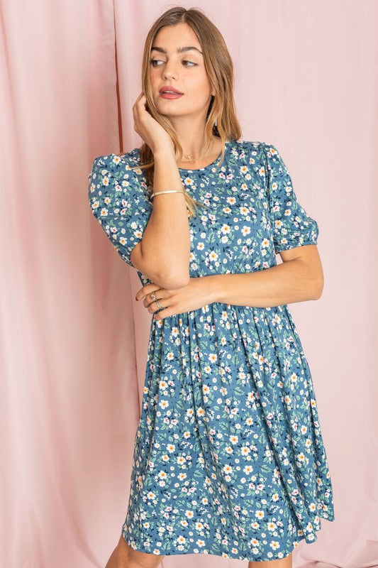 A woman in a Gathered Sleeve Daisy Floral Midi Dress stands in front of a pink curtain, delicately touching her sleeve.