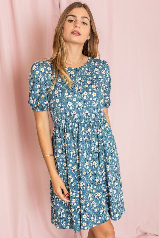 A woman in a Gathered Sleeve Daisy Floral Midi Dress and white ankle boots stands elegantly in front of a pink curtain.