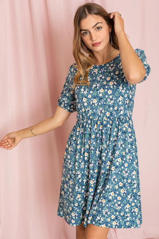 A woman in a Gathered Sleeve Daisy Floral Midi Dress and white ankle boots stands elegantly in front of a pink curtain.