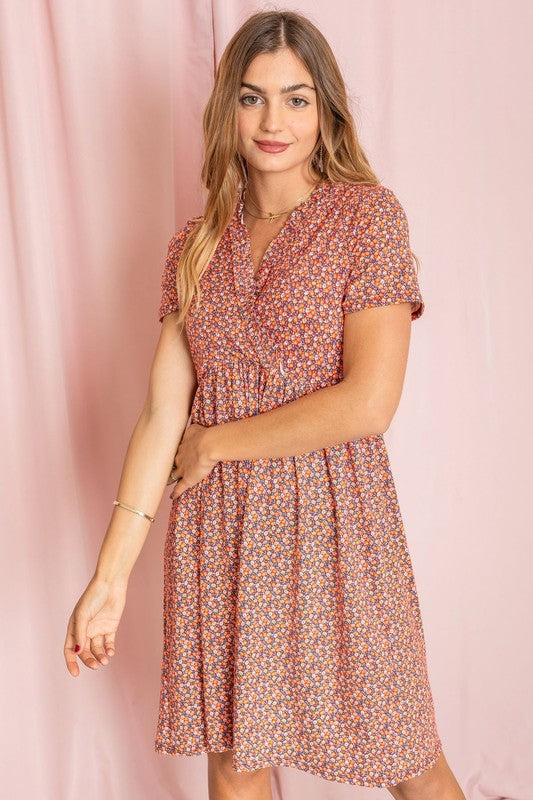 A woman elegantly poses in a Floral Surplice Ruffle Hem Dress, standing gracefully in front of a pink curtain.