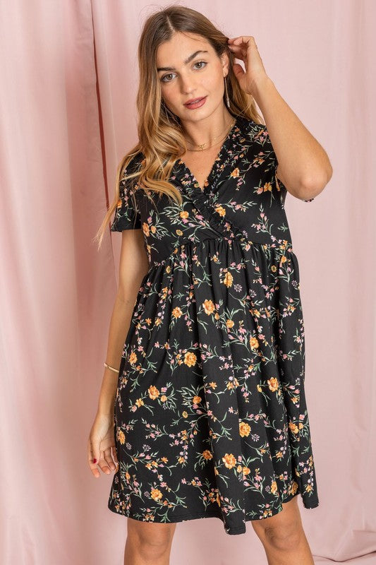 A woman wearing the Floral Surplice Ruffle Hem Dress, crafted in the United States, stands against a pink background, gently touching her hair.