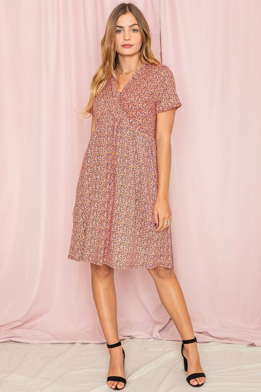 A woman elegantly poses in a Floral Surplice Ruffle Hem Dress, standing gracefully in front of a pink curtain.