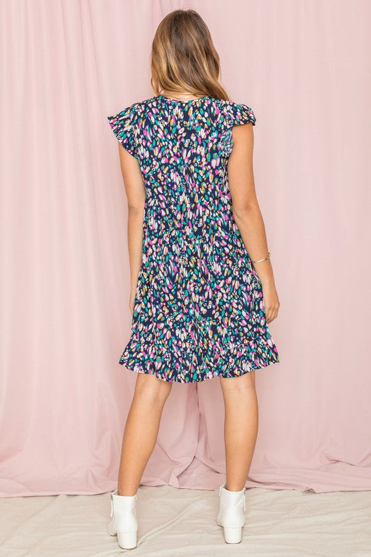 A person stands against a pink background wearing the Colorful Abstract Flutter Sleeve Mini Dress paired with white ankle boots.