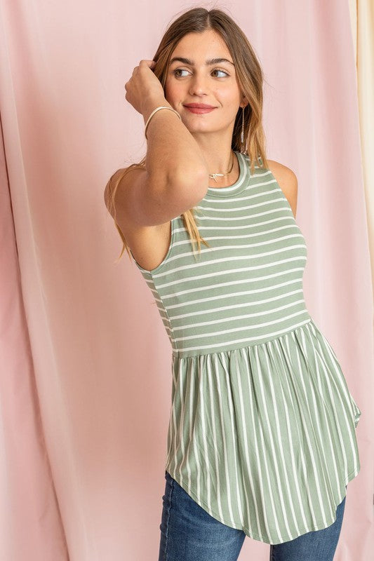 A person in a sleeveless Stripe High Waist Tunic, featuring green and white stripes and crafted in the United States, stands gracefully in front of pastel curtains.