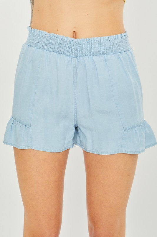 A close-up of a person wearing light blue, high-waisted Woven Solid Shorts with an elastic waistband and ruffled hem, highlighting the breathable fabric for comfortable casual wear.