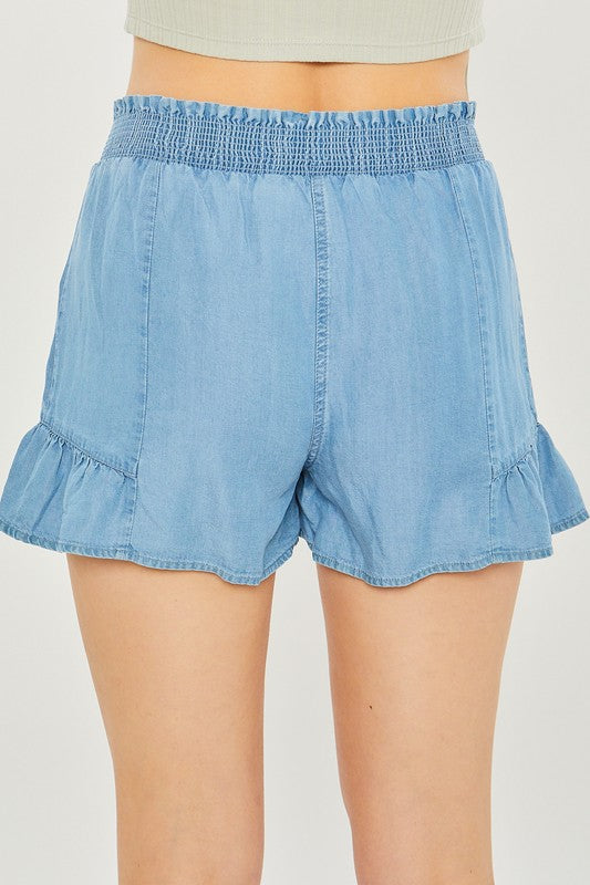 A close-up of a person wearing light blue, high-waisted Woven Solid Shorts with an elastic waistband and ruffled hem, highlighting the breathable fabric for comfortable casual wear.