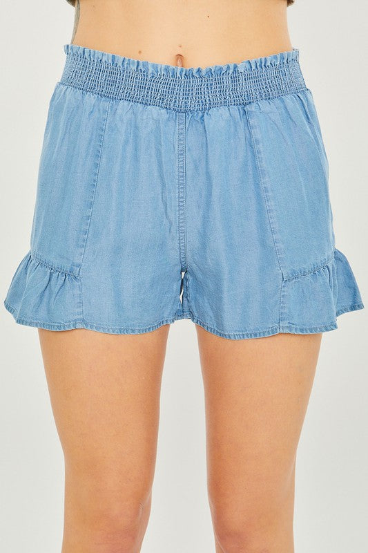 A close-up of a person wearing light blue, high-waisted Woven Solid Shorts with an elastic waistband and ruffled hem, highlighting the breathable fabric for comfortable casual wear.