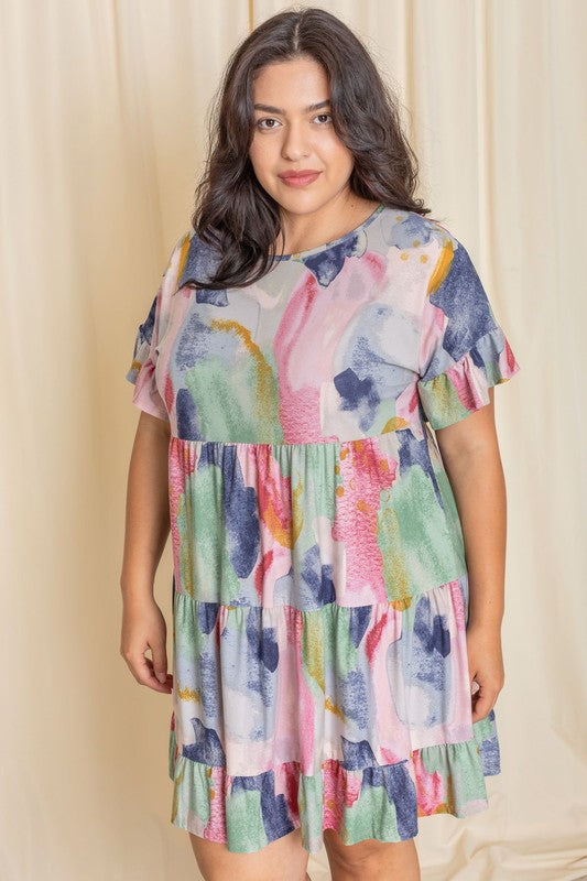 A person wearing a vibrant tie-dye ruffle midi dress and white ankle boots stands in front of a pink backdrop.