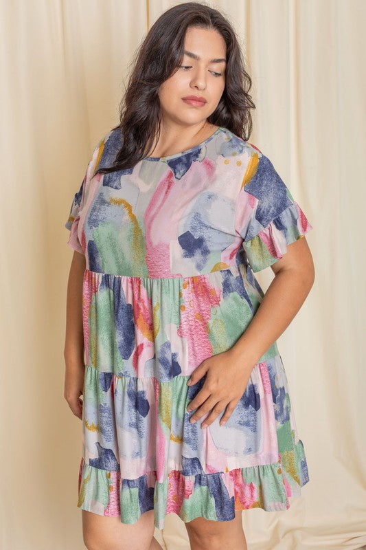 A person wearing a vibrant tie-dye ruffle midi dress and white ankle boots stands in front of a pink backdrop.