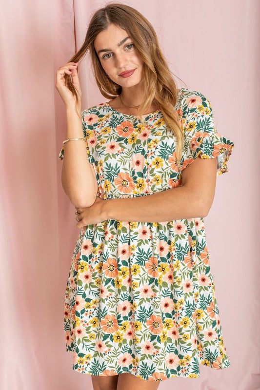 A person wearing the Plus Ditsy Floral Ruffle Chest Pocket Dress stands elegantly against a pink curtain backdrop.