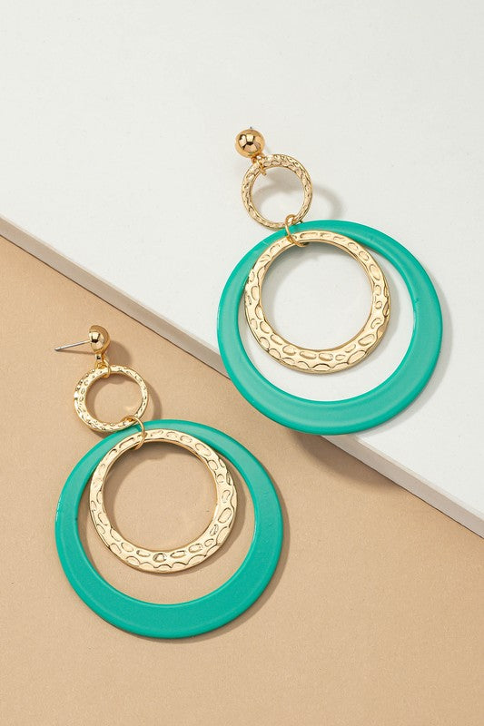 Five pairs of hoop drop earrings featuring hammered metal and vibrant acrylic accents are displayed against a beige and white backdrop, highlighting their shiny gold plating.
