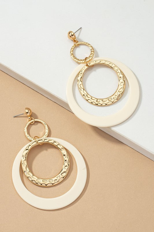 Five pairs of hoop drop earrings featuring hammered metal and vibrant acrylic accents are displayed against a beige and white backdrop, highlighting their shiny gold plating.