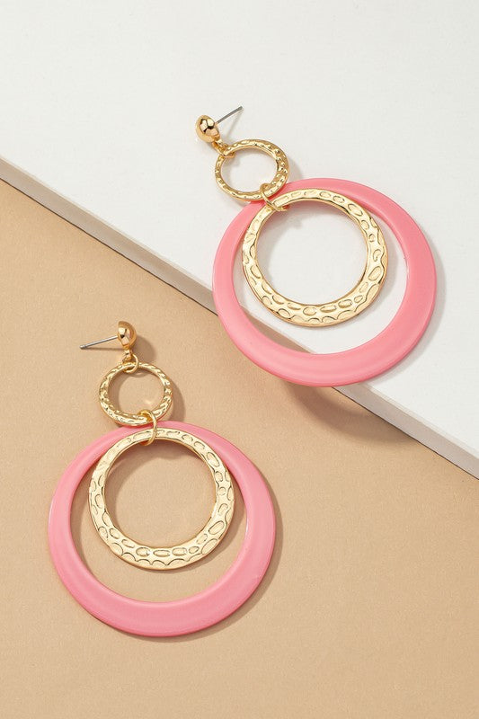 Five pairs of hoop drop earrings featuring hammered metal and vibrant acrylic accents are displayed against a beige and white backdrop, highlighting their shiny gold plating.