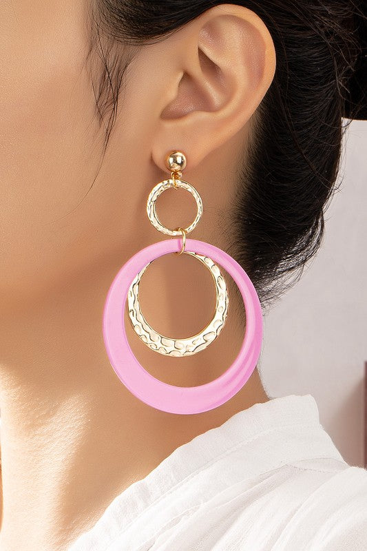 Five pairs of hoop drop earrings featuring hammered metal and vibrant acrylic accents are displayed against a beige and white backdrop, highlighting their shiny gold plating.