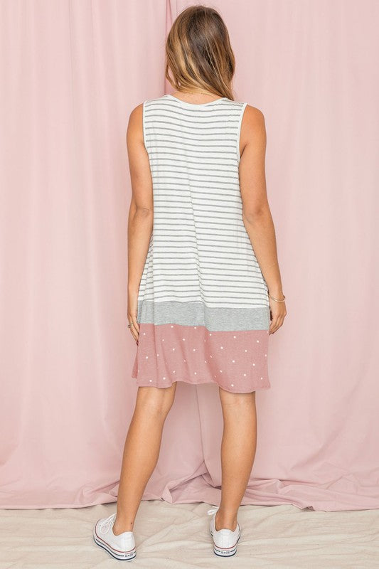 A person is wearing the "Stripe A-Line Color Block Midi Dress," featuring white and gray stripes, with a light blue polka-dotted hem, set against a pale pink background.