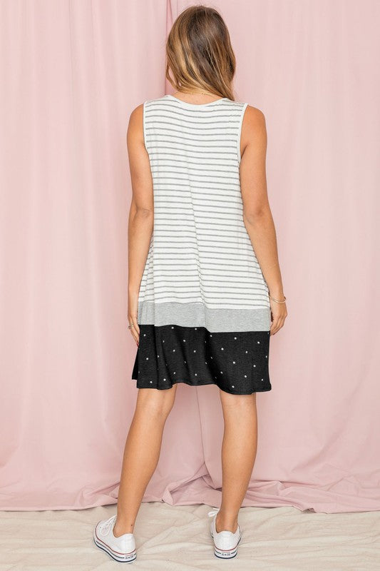 A person is wearing the "Stripe A-Line Color Block Midi Dress," featuring white and gray stripes, with a light blue polka-dotted hem, set against a pale pink background.