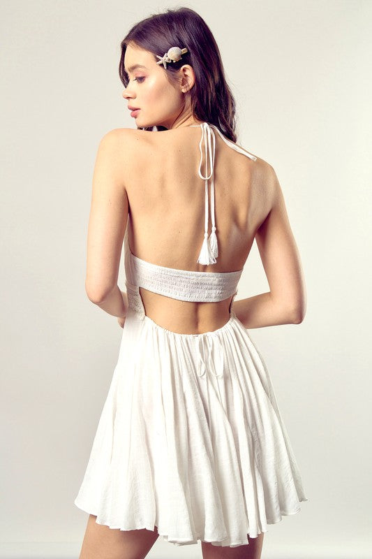 A person dressed in the Lace Trim with Back Drawstring Dress, featuring a sleeveless design, a white pleated skirt, and intricate lace trim, gazes to the side against a neutral backdrop.