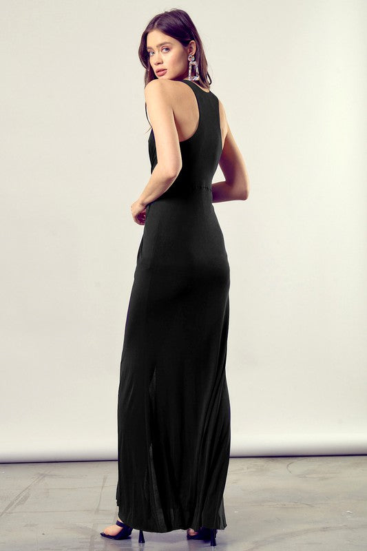 A woman dressed in a Twist-Front Side Leg Slit Knit Dress, featuring a long black design with a deep V-neckline and side leg slit.