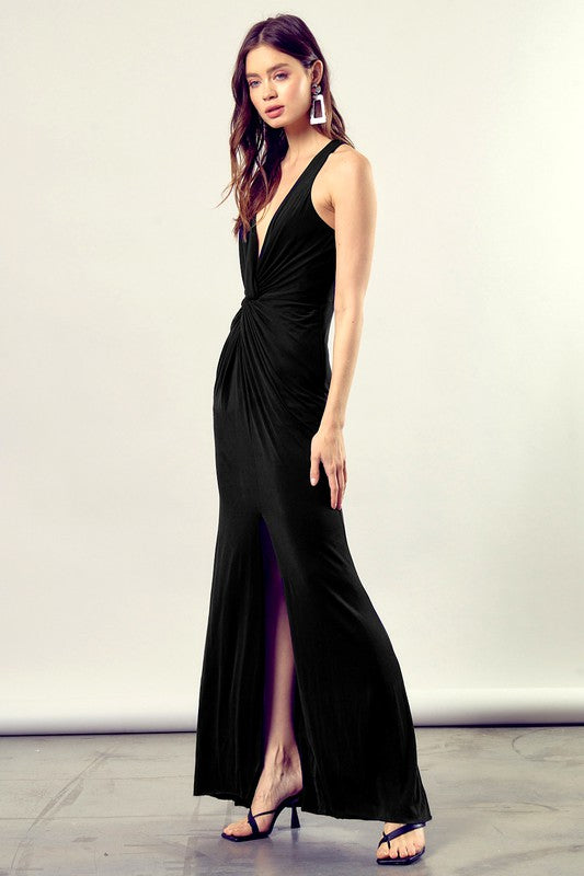 A woman dressed in a Twist-Front Side Leg Slit Knit Dress, featuring a long black design with a deep V-neckline and side leg slit.