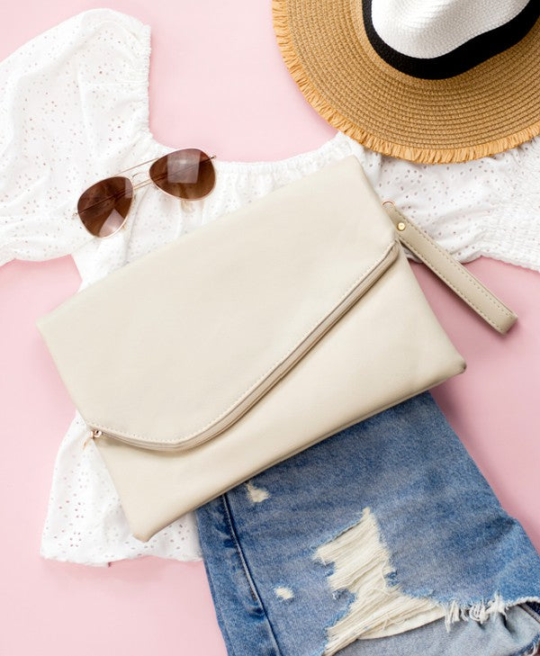 A woman in a white top holds the Foldover Envelope Clutch in black while sitting.