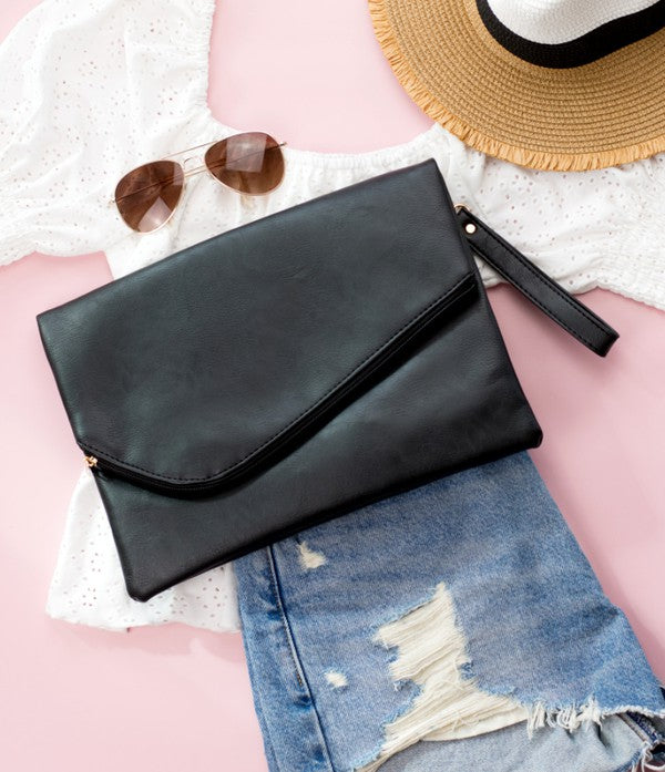 A woman in a white top holds the Foldover Envelope Clutch in black while sitting.