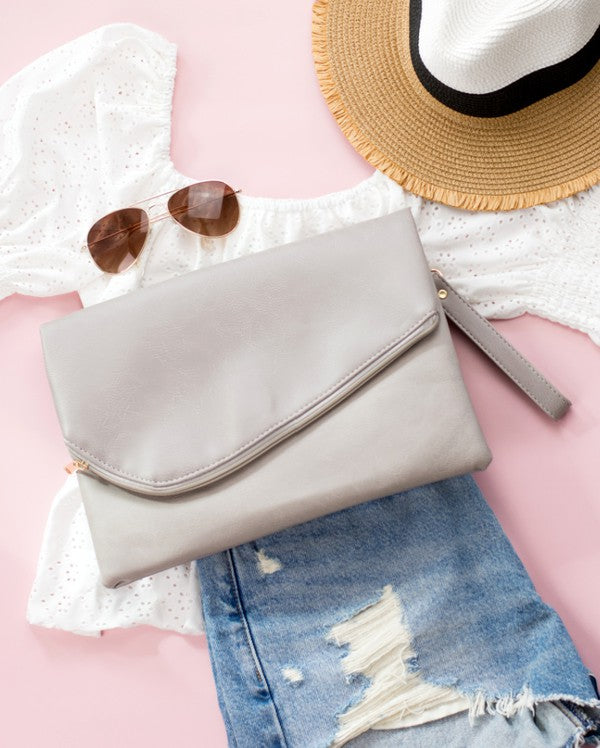 A woman in a white top holds the Foldover Envelope Clutch in black while sitting.